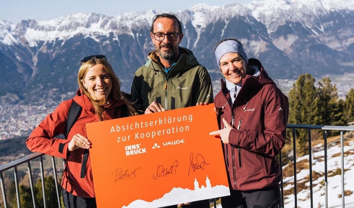 Verantwortliche von Innsbruck Tourismus und VAUDE posieren für ein Foto vor Alpenkulisse